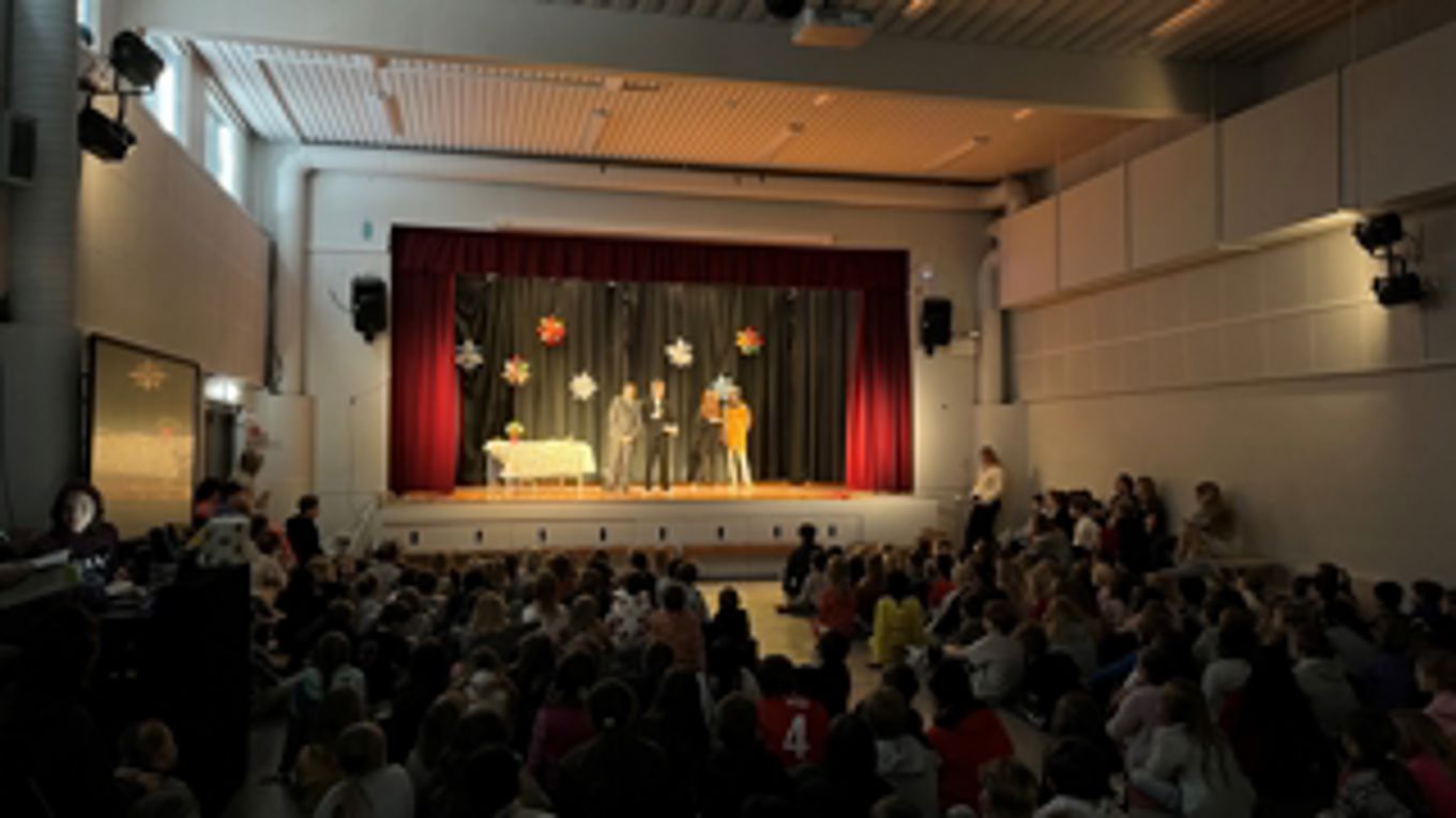 Foto: SA en gruppe mennesker som sitter i et rom med en scene og et gardin